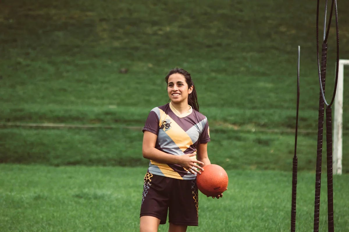 Young woman with all in her hand in grassy field playing quidditch
