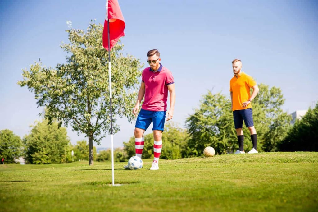 Two men playing footgolf, with one ready to kick ball in hole.

