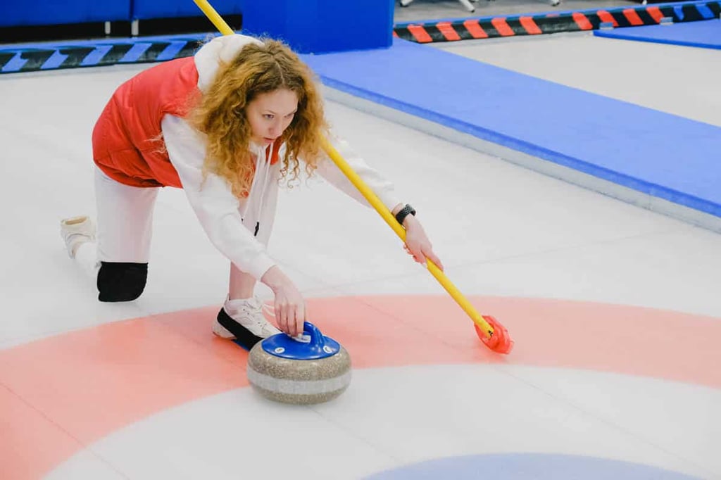woman on ice curling with stone in her hand getting ready to slide it

