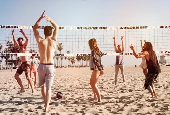 young adults playing beach volleyball with all their hands in the air and ball on the gound