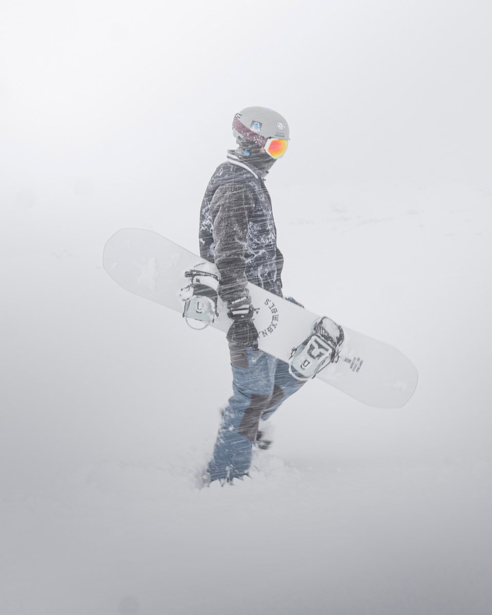 Lone snowboarder in powdery snow holding snowboard under arm
