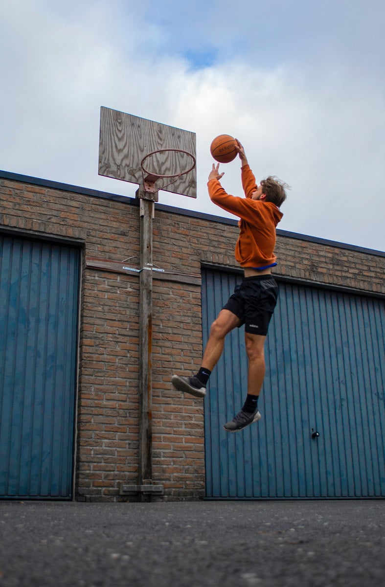 Man jumping up to dunk basketball on hoop with no net
