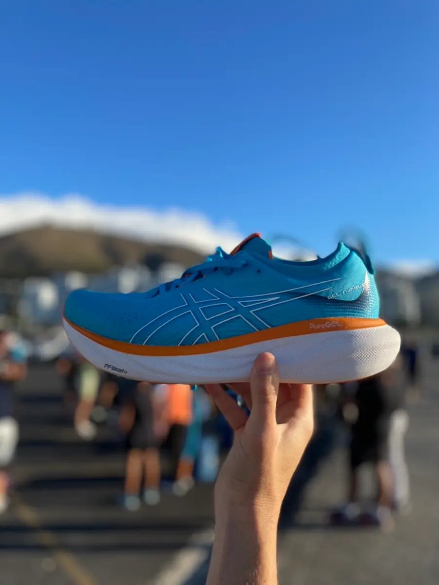closeup of ASICS Gel-Nimbus 25 being held up by a hand with blurred out crowd in background