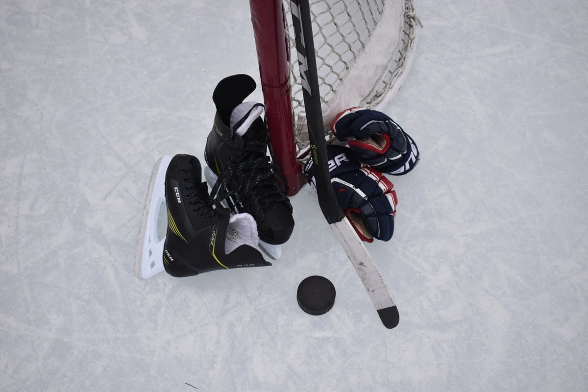Hockey skates, glvoes, puck and stick lying on ie near goal post
