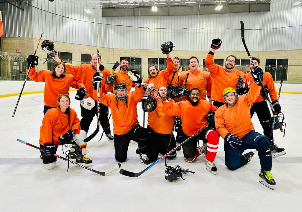 John's team hockey photo on the ice with the group in orange jerseys pumping hands up in the air