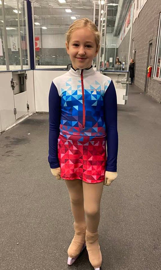 John's daughter at the ice rink in figure skating outfit and skates posing for photo