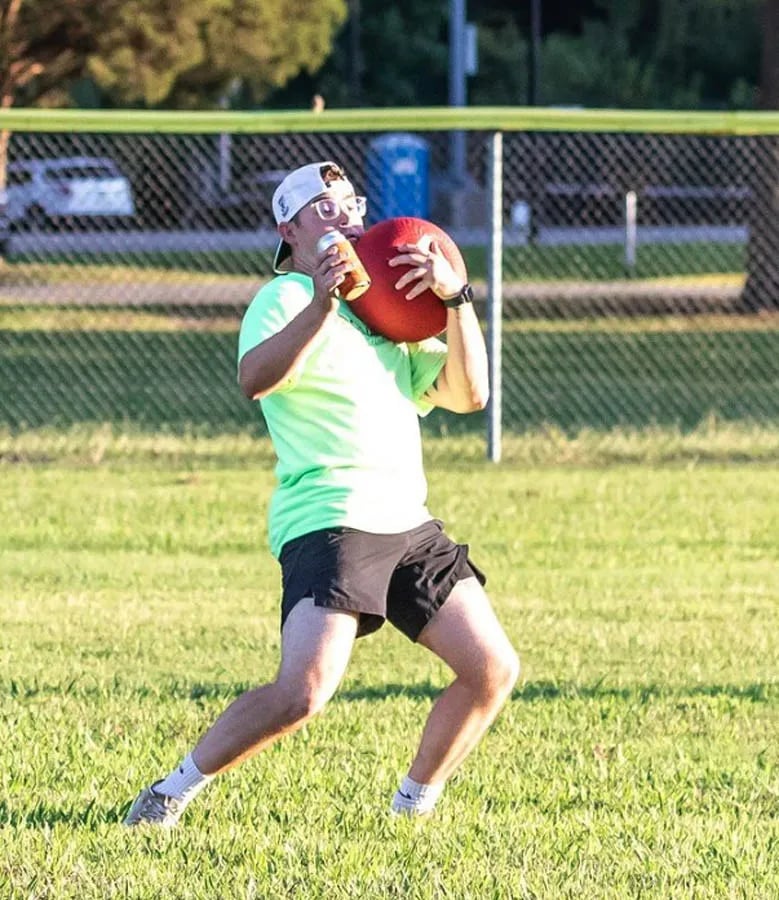 Man in lime green t-shirt catching a kickball while holding a can of beer