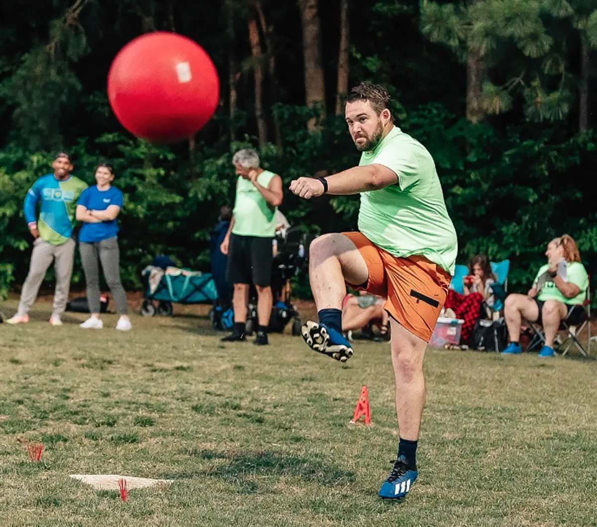 man in lime green shirt with one leg raised after just kicking a kickball
