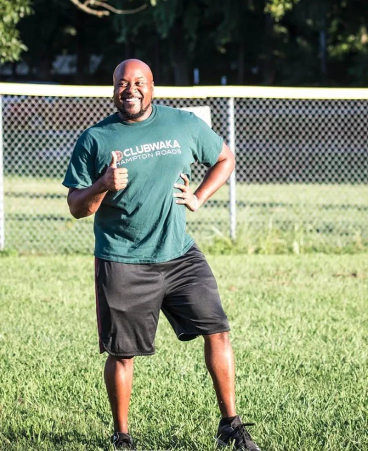 man in dark green t-shirt and black shorts on grassy field giving thumbs up sign