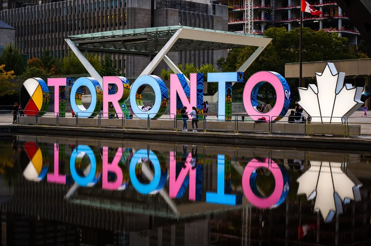 Downtown Toronto with neon pink and blue Toronto sign reflecting in the water