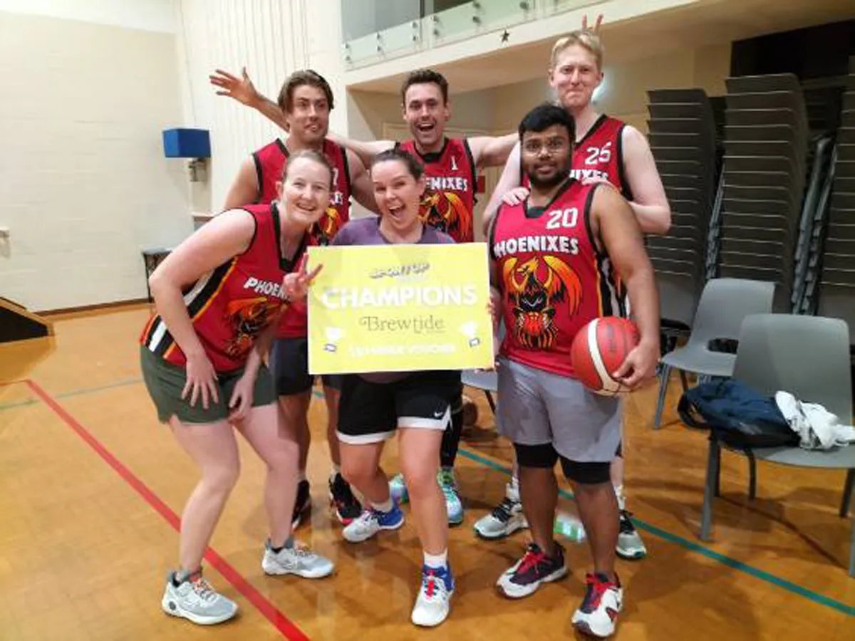 Over 30s basketball team with four men and two women holding up a "Champions" sign.
