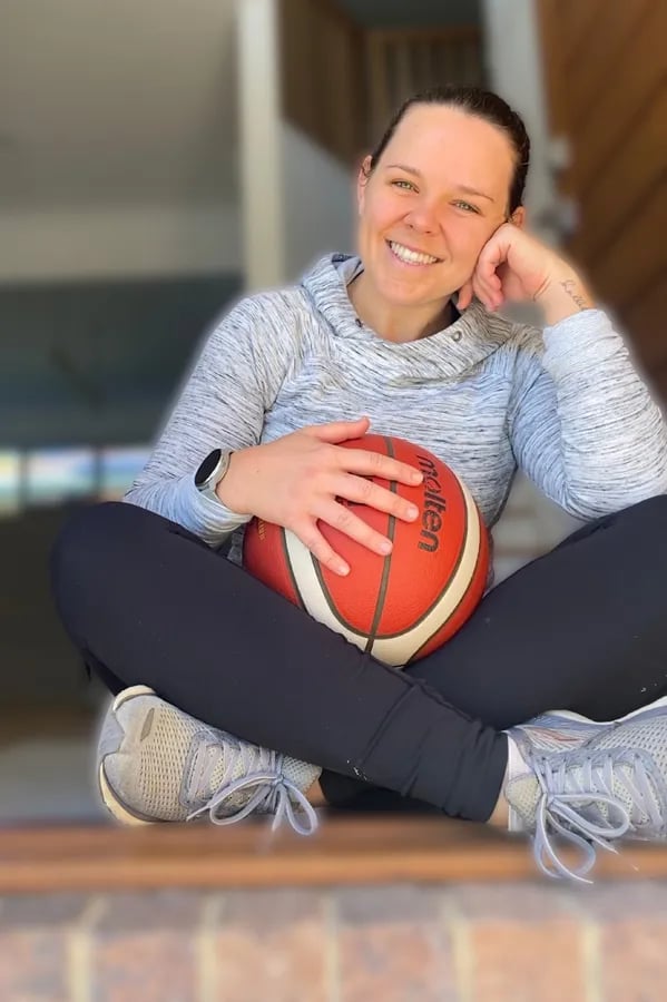woman sitting cross legged on ground holding a basketball on her lap