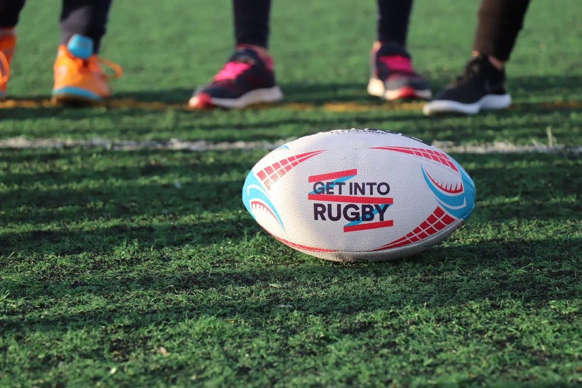 closeup of a rugby ball on the pitch that says "get into rugby" on it