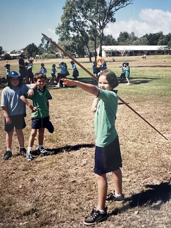 young girl holding a javelin in one arm as if ready to throw