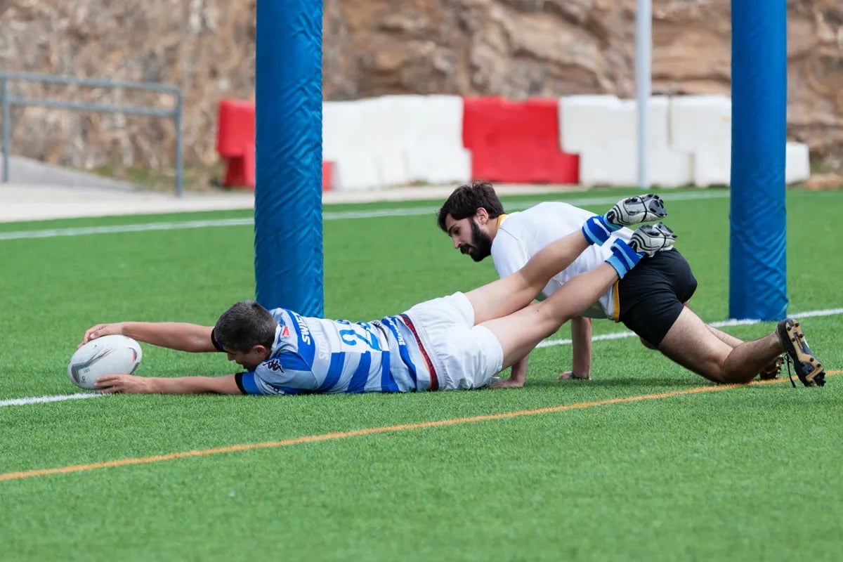 Two male rugby players on ground, one outstretched with ball in hands reaching over goal line