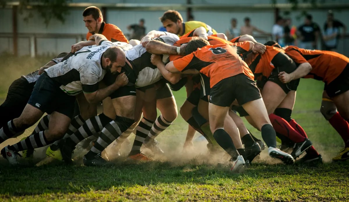male rugby players from opposing teams in scrum formation with dirt kicking up from the grass by their feet