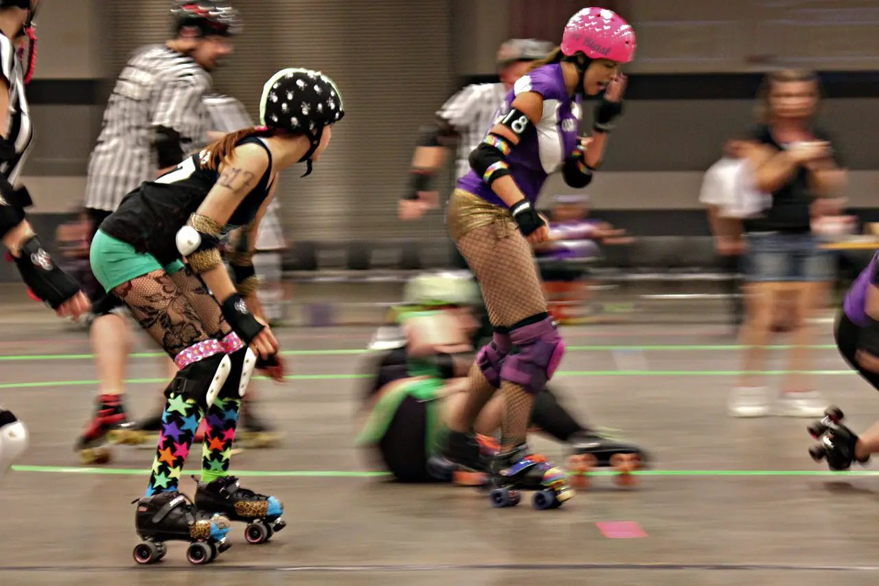 women playing roller derby skating around track. Two women clear in foreground with background blurred.'