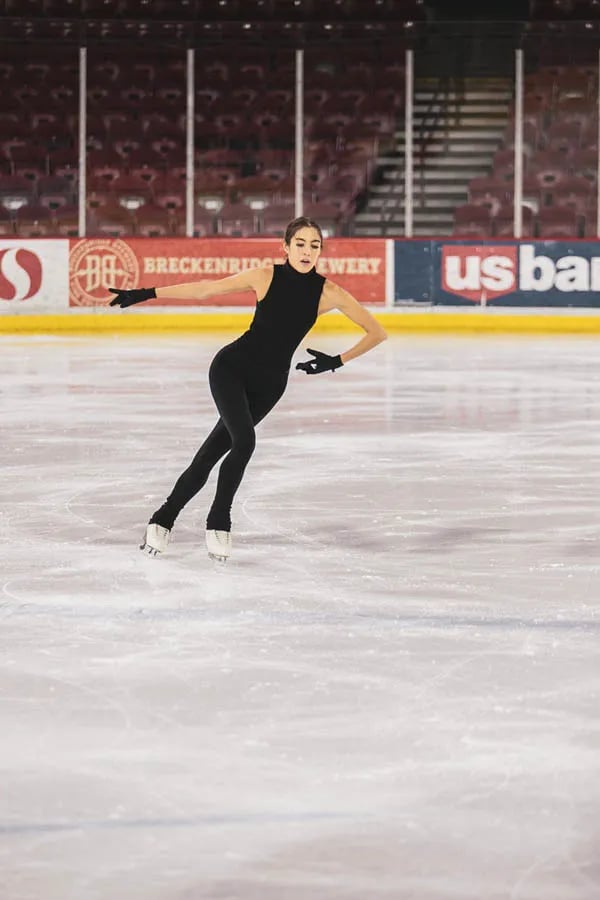 brunette female figure skater in black tank top and pans with black gloves gliding on ice