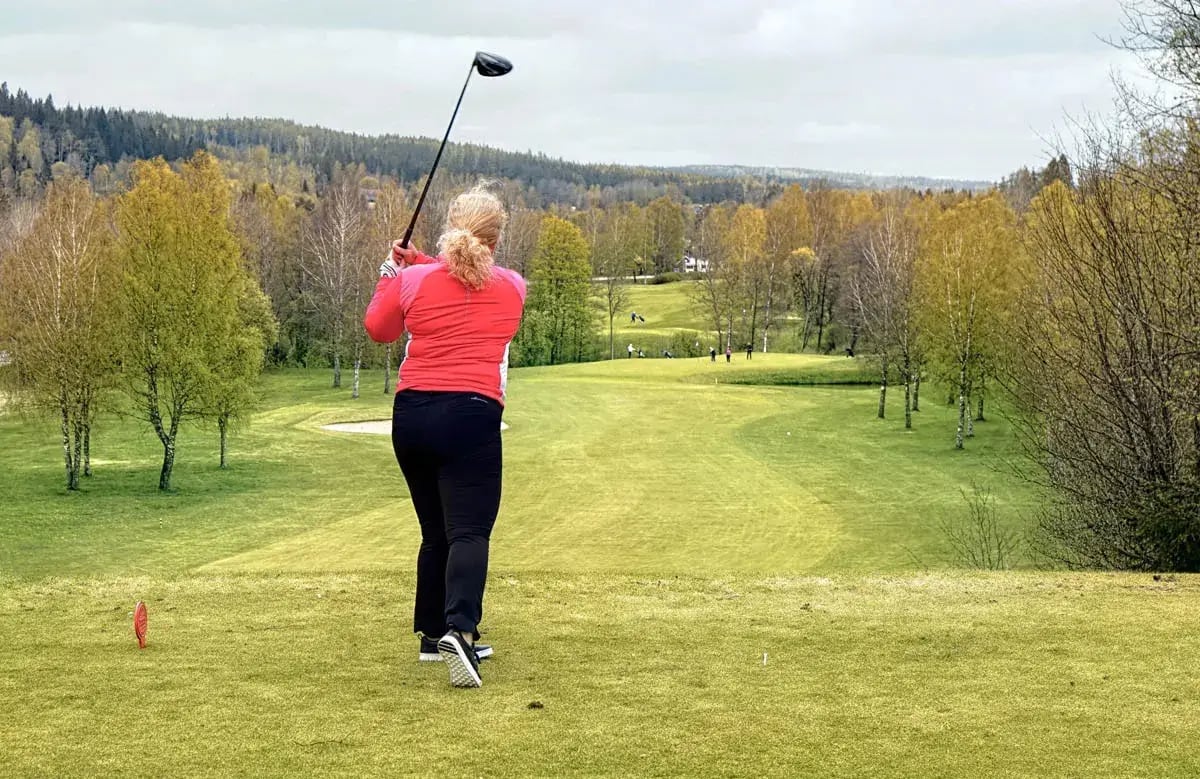 woman in red top and black pants on golf course tee after she just hit ball with her driver