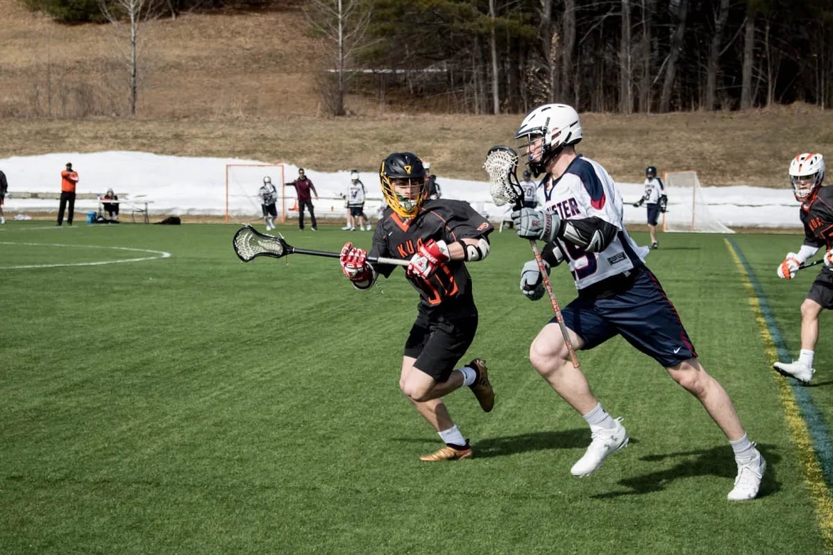 male lacrosse players on turf field in an action shot from opposing teams