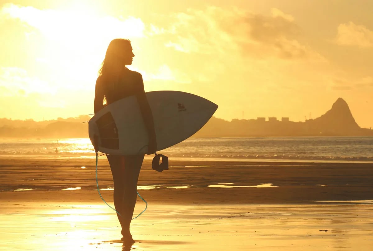 surfer holding board on beach at sunset