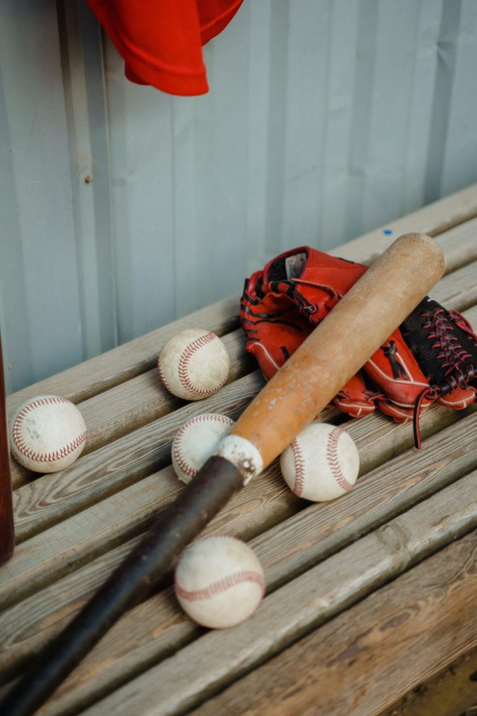 Dugout with closeup of baseball bat and 5 balls on the bench with a glove.