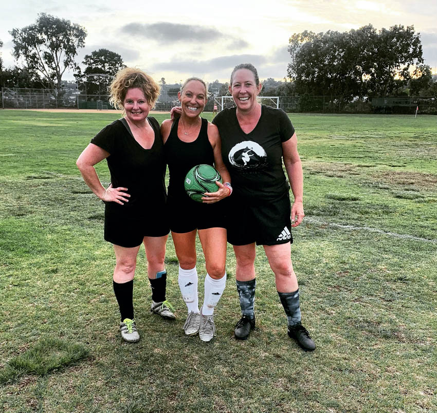 three woman posing on soccer field with soccer ball