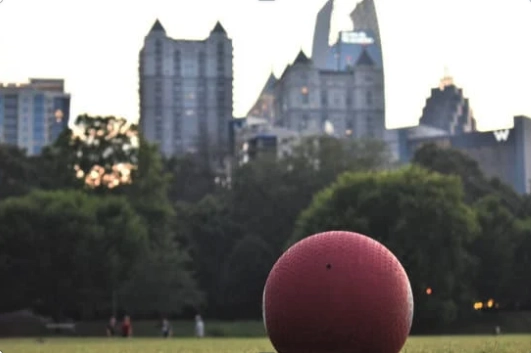 kickball in foreground on grass with cityscape behind it