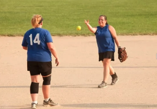 two women on softball field with one tossing the ball to the other