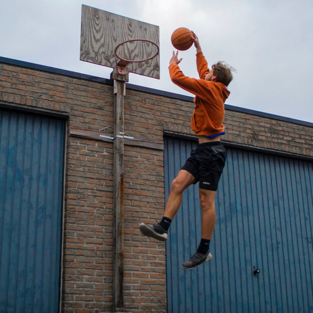 Man jumping up to dunk basketball on hoop with no net
